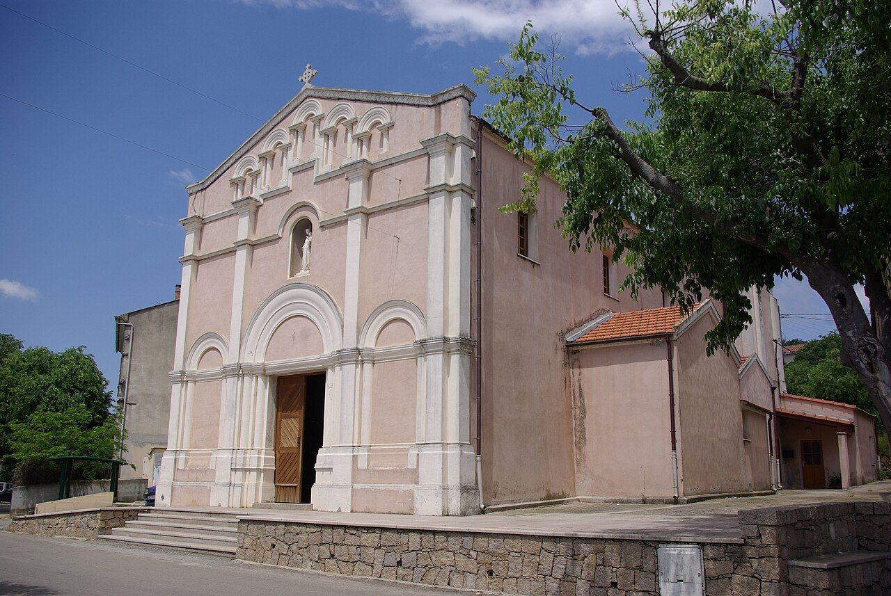 L'église du centre d'Afa, façade rose et blanche à arcades, au-dessus d'un muret de pierre, sous un ciel bleu
