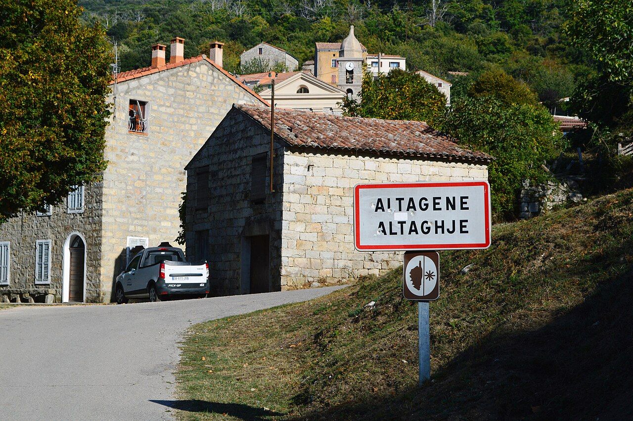 L’entrée d’Altagène : panneau bilingue « Altagene – Altaghjè », maisons de granite et clocher de l’église dans la verdure