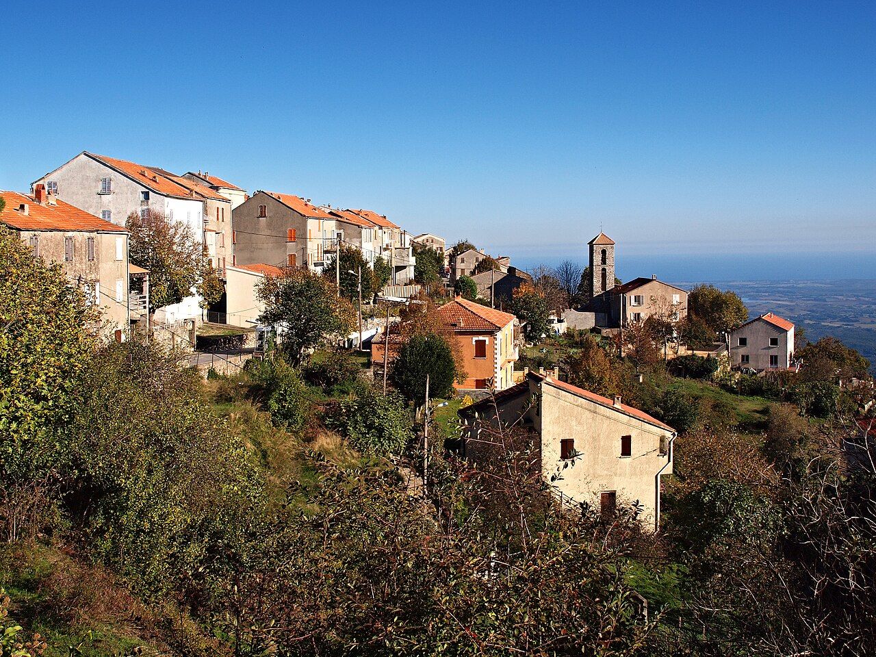 Maisons du village d’Antisanti étagées sur la crête, avec le clocher de l’église et la plaine orientale au loin