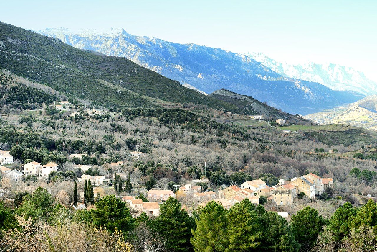 Le village de Casanova au milieu des arbres, au pied de collines boisées et de montagnes enneigées au loin
