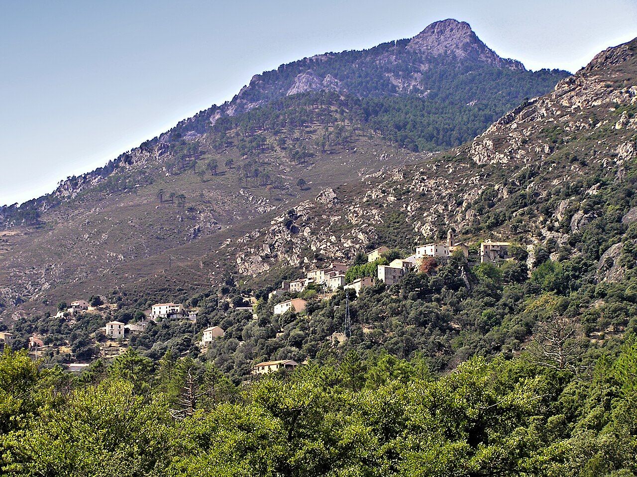 Le village de Castirla, maisons étagées sur un versant de maquis et de chênes, sous une montagne rocheuse