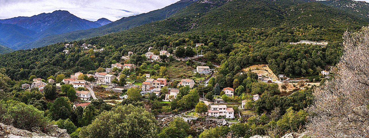 Le village de Chisa vu depuis l'est, ses maisons dispersées à flanc de montagne au milieu des arbres, avec des sommets au fond