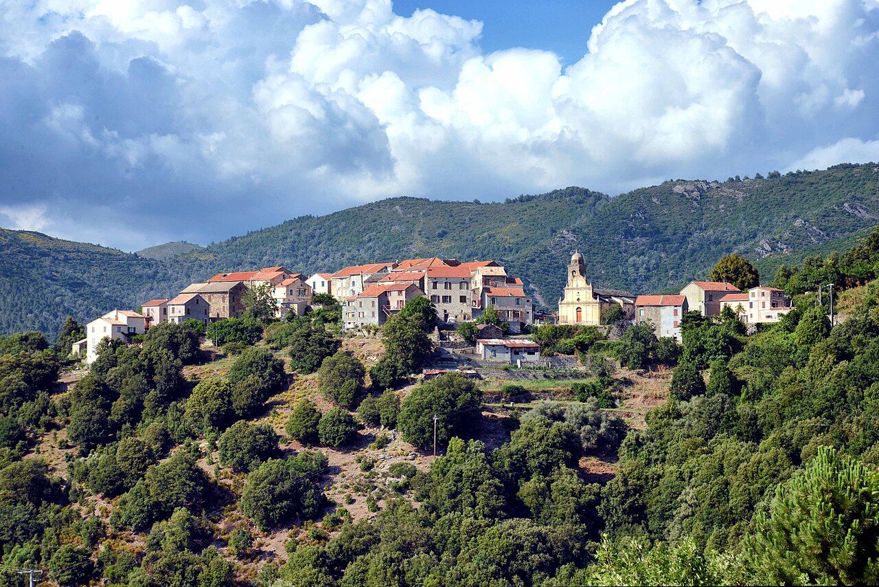 Le village de Focicchia, maisons aux toits rouges et église Saint-Blaise alignées sur une crête boisée, sous un ciel nuageux