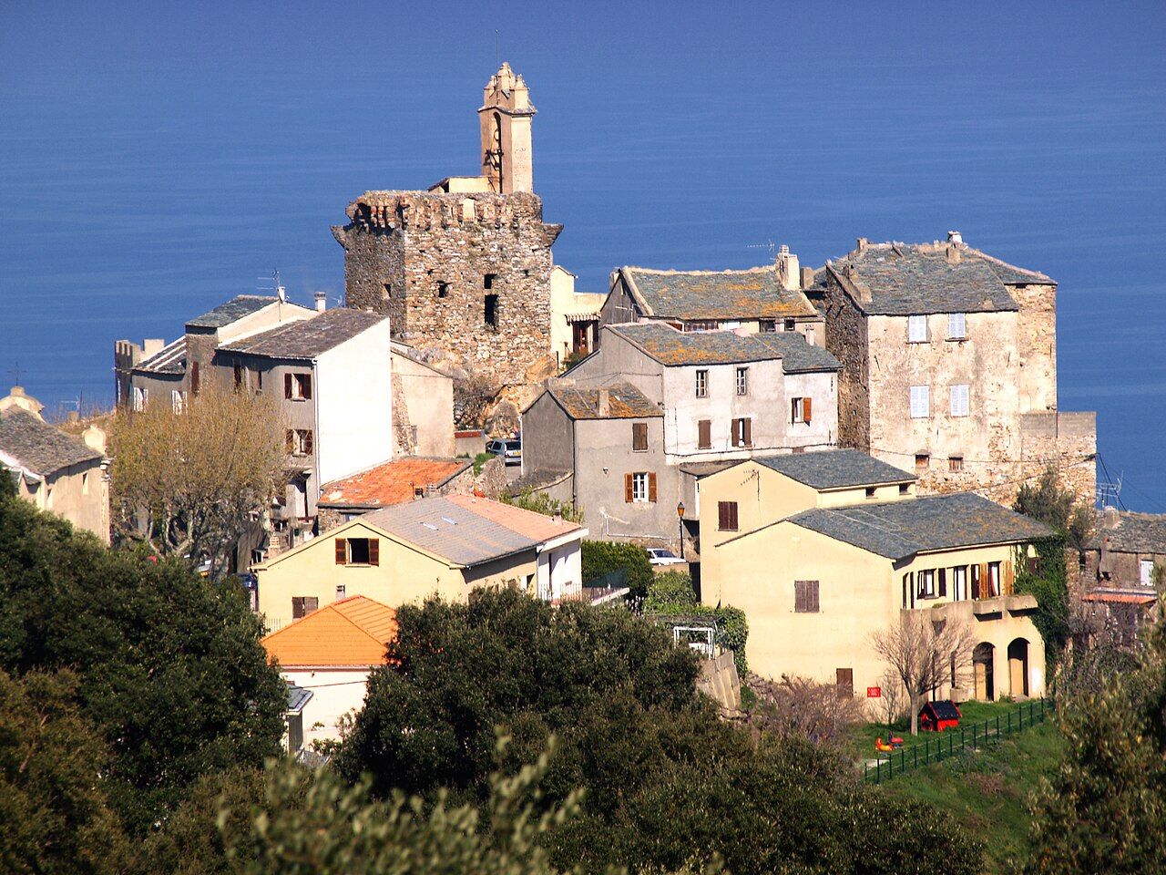 Le vieux village de Furiani groupé autour de sa tour carrée surmontée d'un clocher, avec la mer en arrière-plan