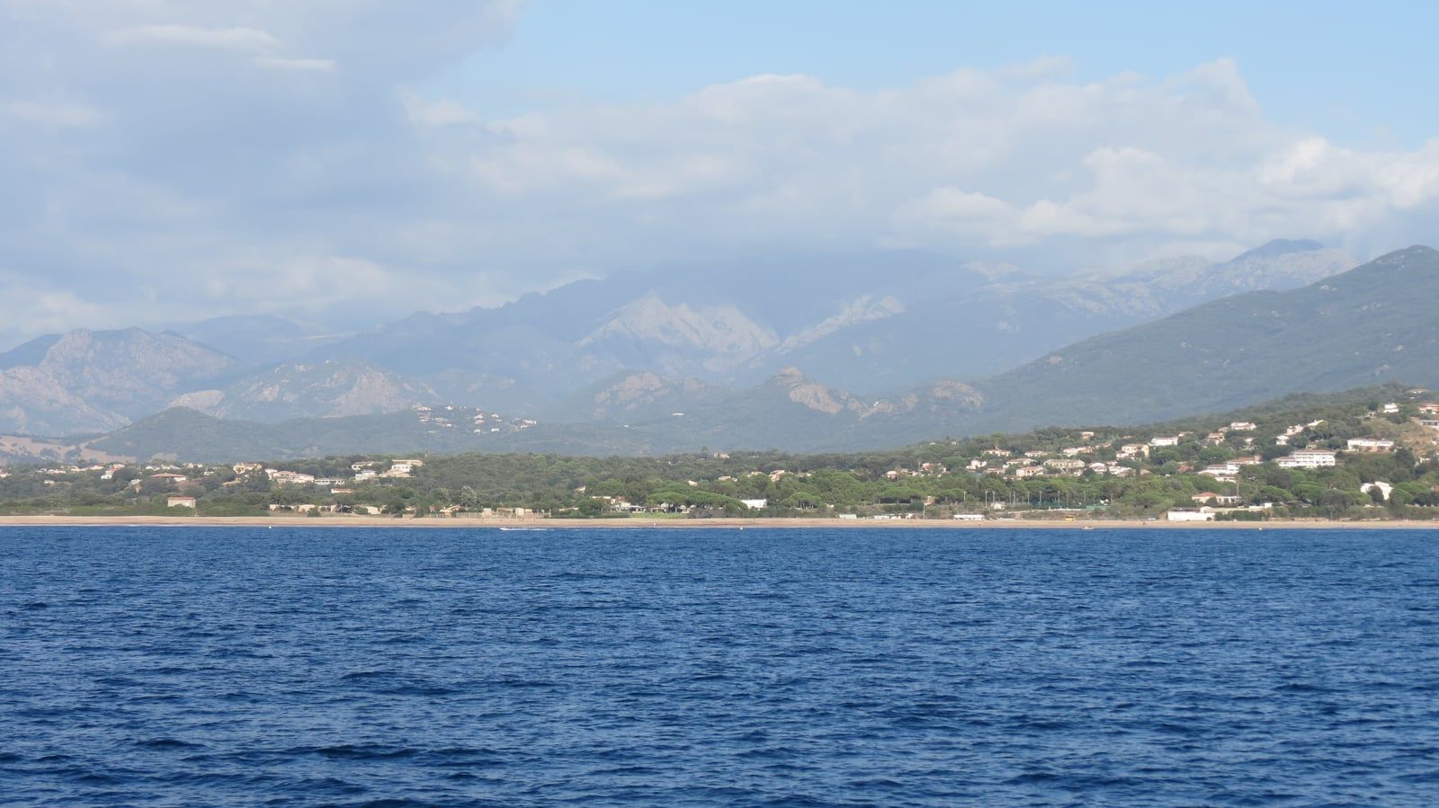 La station balnéaire de Porticcio vue du golfe d'Ajaccio : longue plage, maisons dans les pins et montagnes en arrière-plan