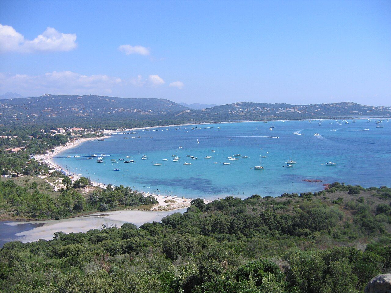 Le golfe de San Ciprianu vu des hauteurs : longue plage de sable, eau turquoise, bateaux au mouillage et collines couvertes de maquis