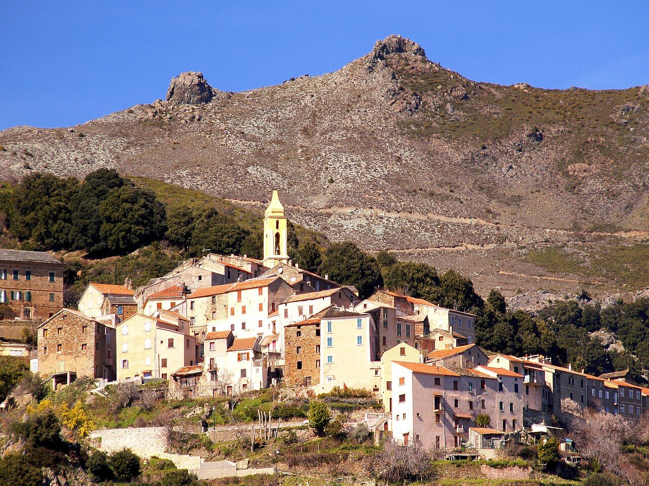 Le village de Lento, ses hautes maisons et le clocher de son église, au pied d’une montagne rocheuse