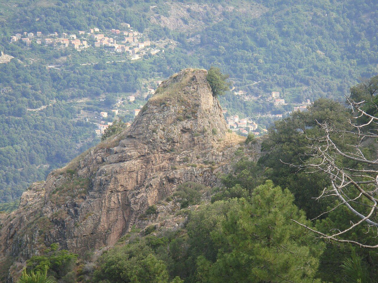 Les ruines du fort de la Zurlina sur un éperon rocheux, avec les maisons de Letia étagées sur le versant boisé en arrière-plan