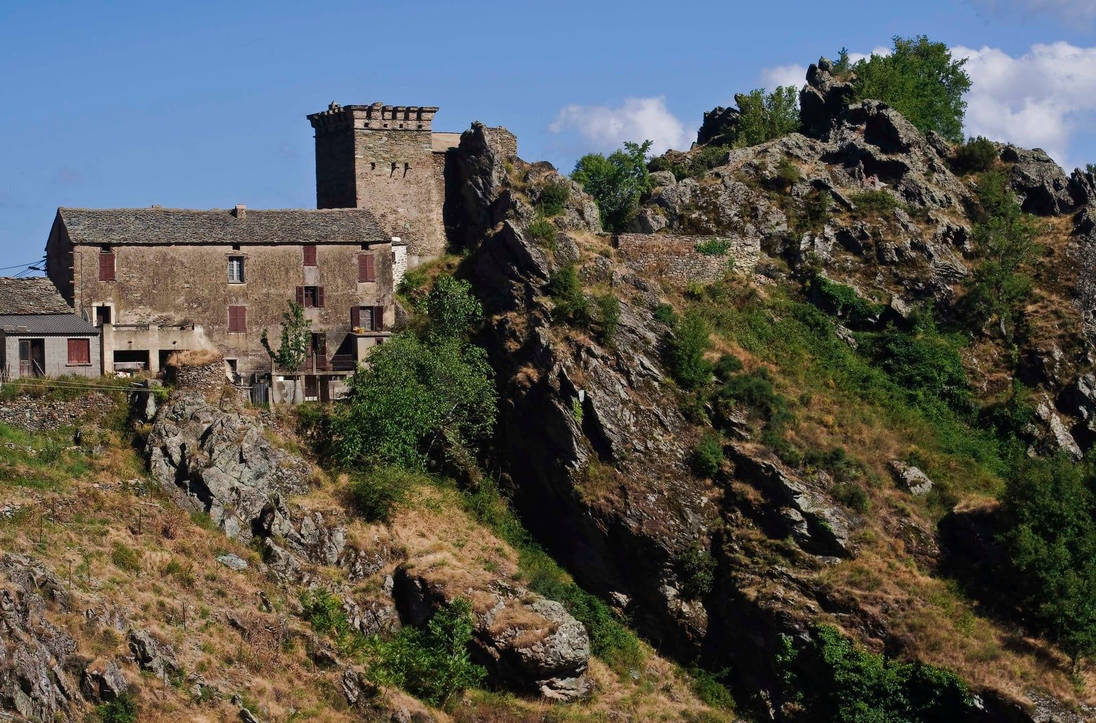 Maisons anciennes de Matra et une tour crénelée en pierre, au bord d’un éperon rocheux couvert de maquis