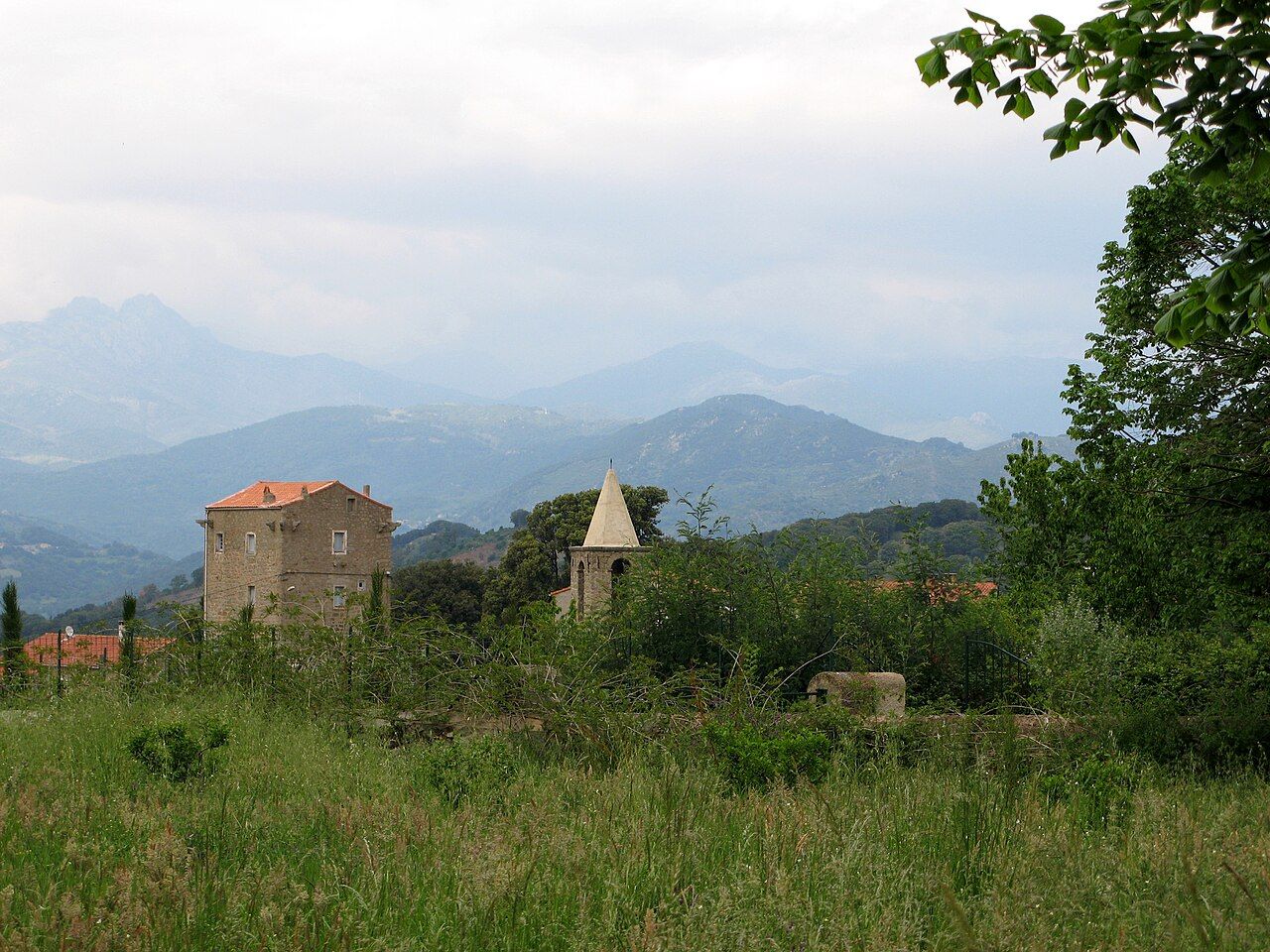 Une haute maison carrée et un clocher pointu à Petreto-Bicchisano, devant les montagnes de l’intérieur