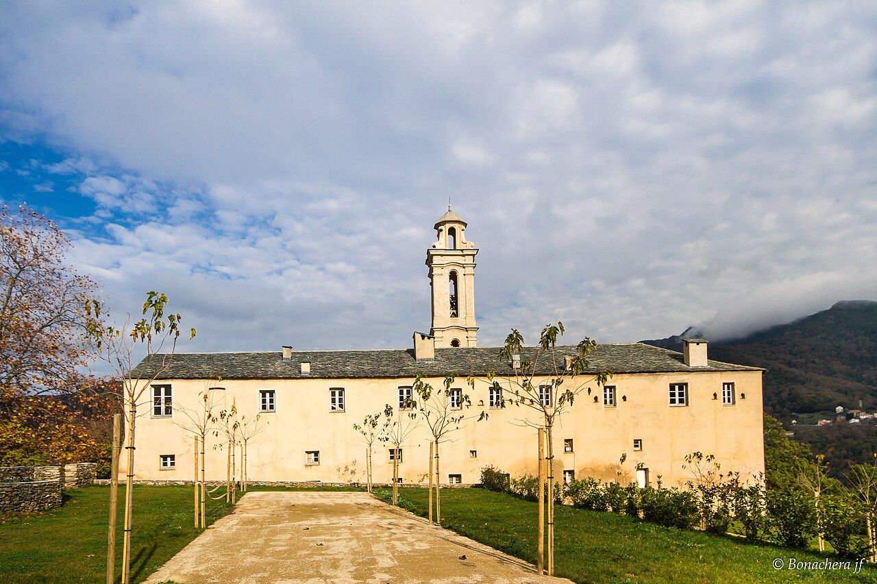 Le couvent d’Alesani à Piazzali, long bâtiment ocre surmonté d’un clocher, vu depuis le chemin d’accès bordé de jeunes arbres