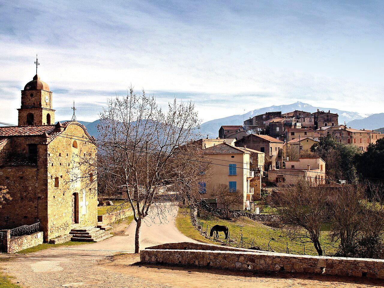 L’église Saint-Michel de Piedigriggio au premier plan et les maisons du village, avec des montagnes enneigées au loin