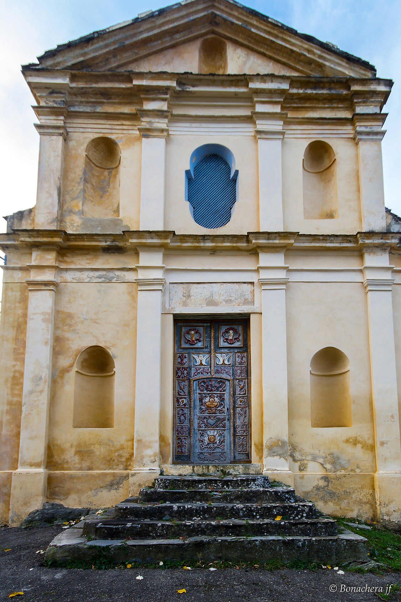 La façade de l’église Saint-Bernardin de Piedipartino et sa porte sculptée et peinte, au sommet d’un escalier de pierre
