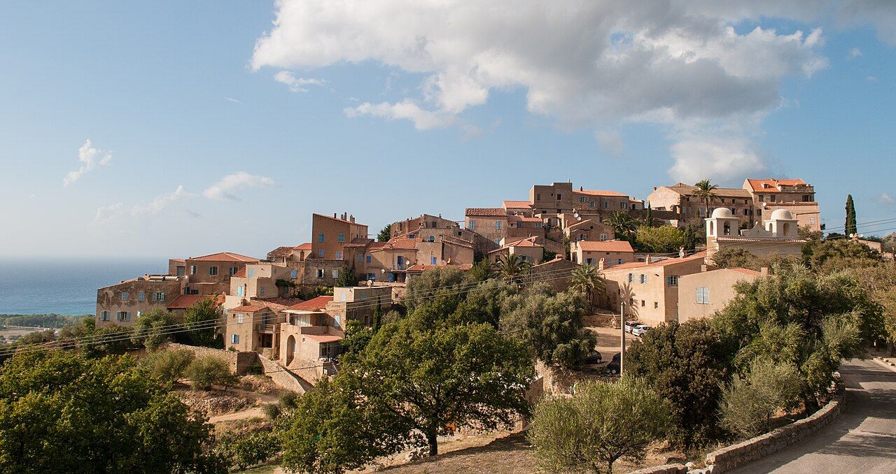 Le village perché de Pigna, maisons ocre aux toits de tuiles et église à deux clochers ronds, entouré d'oliviers, avec la mer au loin