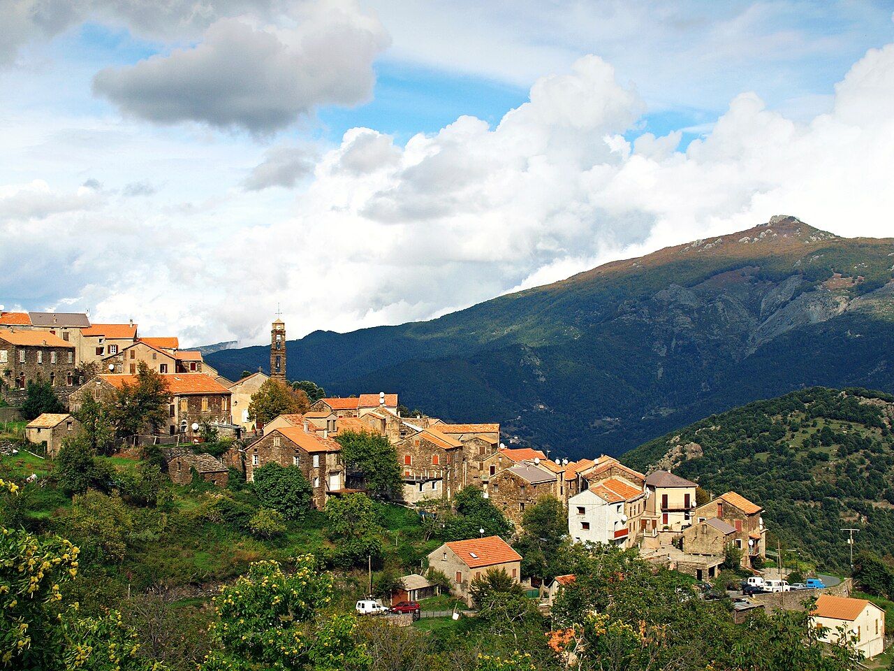 Le village de Rusio, ses maisons de pierre aux toits orangés et son clocher sur une arête, avec le mont San Petrone en arrière-plan