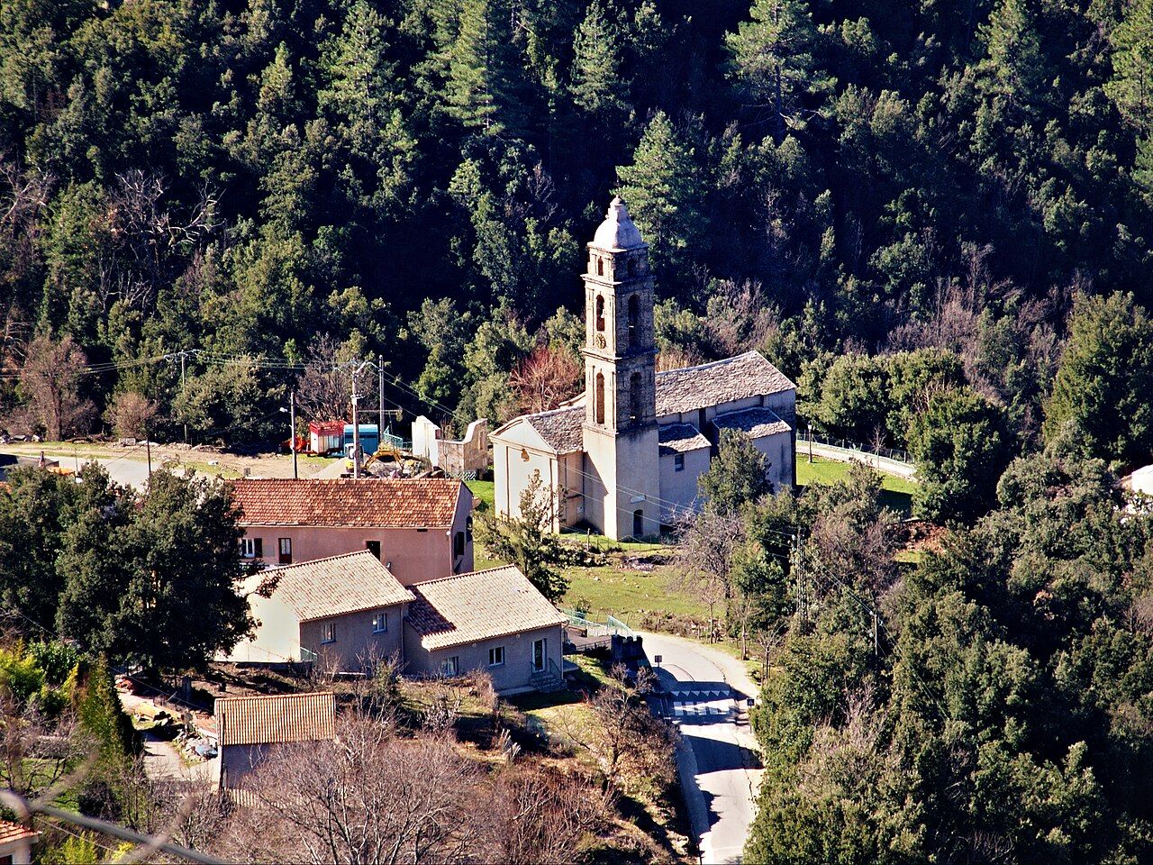 L’église San Lorenzo et son haut clocher au hameau de Tribbio, entourés de maisons aux toits de lauzes et de bois de chênes verts