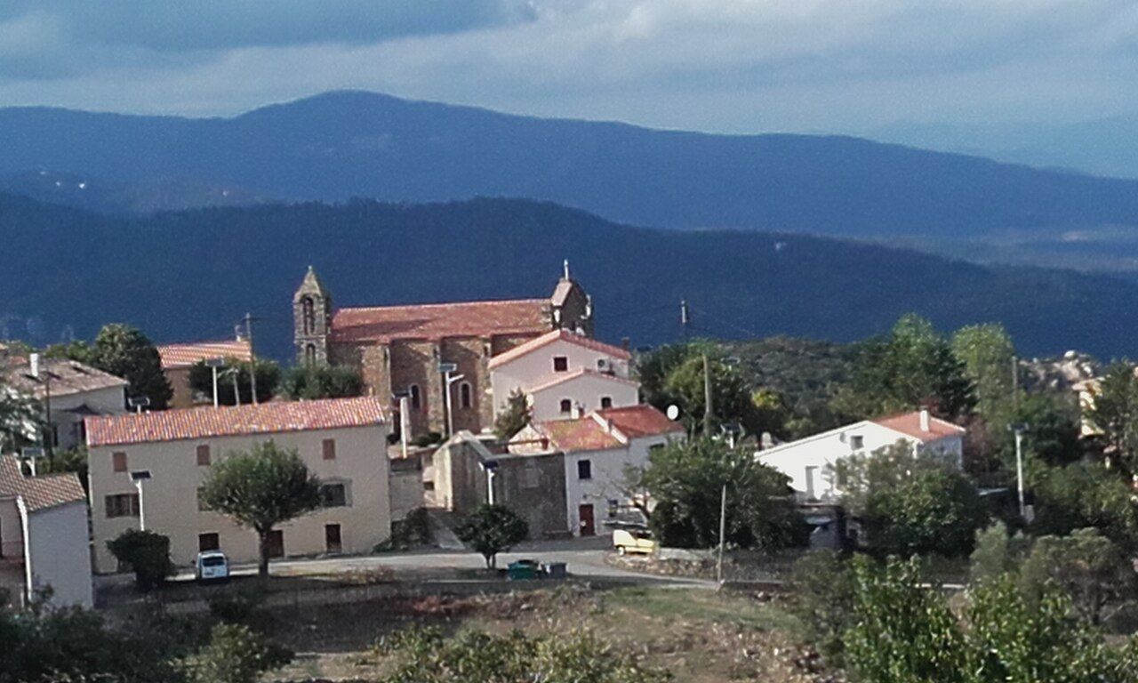 Le village de Sari et son église, devant des collines boisées et des montagnes