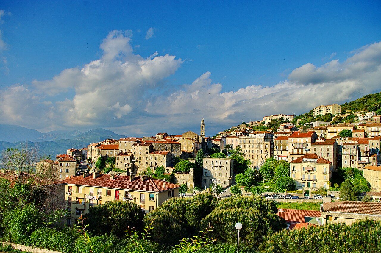 La vieille ville de Sartène, maisons de granit et clocher de l'église Sainte-Marie, accrochées à la colline sous un ciel bleu, montagnes au loin