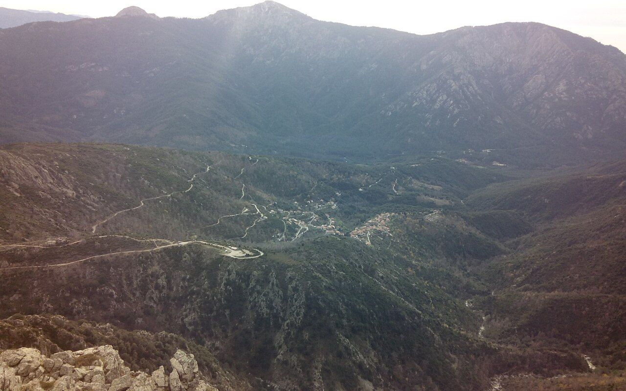 Le village de Soccia vu depuis Favarone : maisons groupées au creux d’une vallée boisée, sous une ligne de montagnes