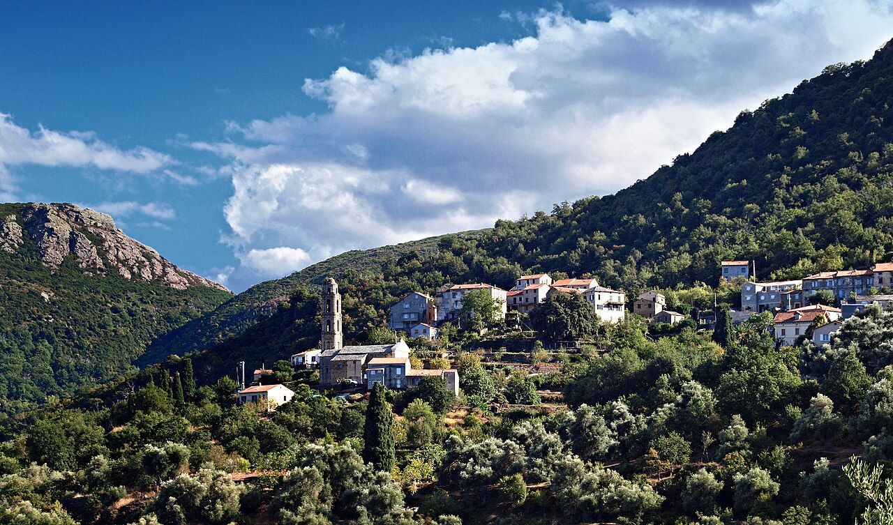 Le village de Sorio accroché à la pente boisée, avec le haut clocher de l’église San Filippu Neri et les rochers de la Serra di Tenda