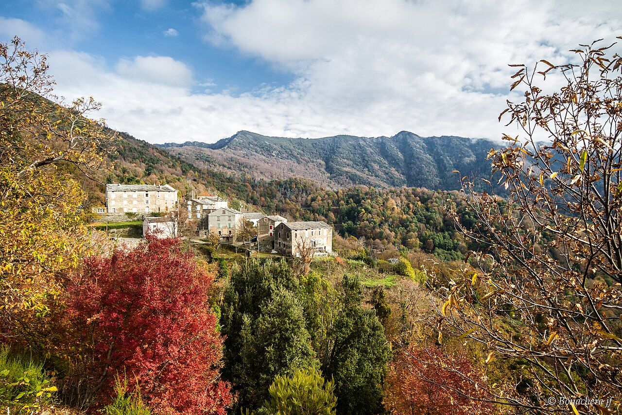 Les maisons de pierre de Tarrano sur un versant boisé aux couleurs d’automne, devant une montagne de la Castagniccia