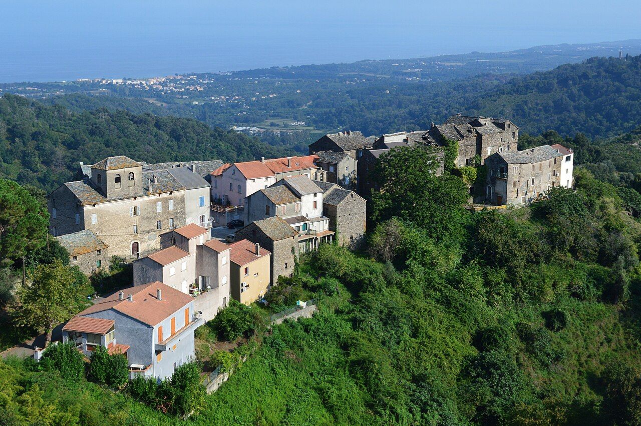 Le hameau d’Orneto, maisons de pierre et toits de tuiles sur une crête boisée, avec la plaine orientale et la mer à l’horizon