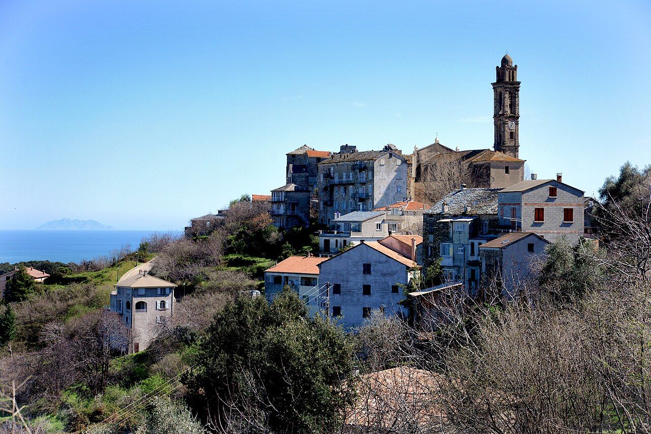 Le village de Venzolasca sur son éperon, dominé par le haut clocher de l’église Santa Lucia, avec la mer et une île de l’archipel toscan à l’horizon