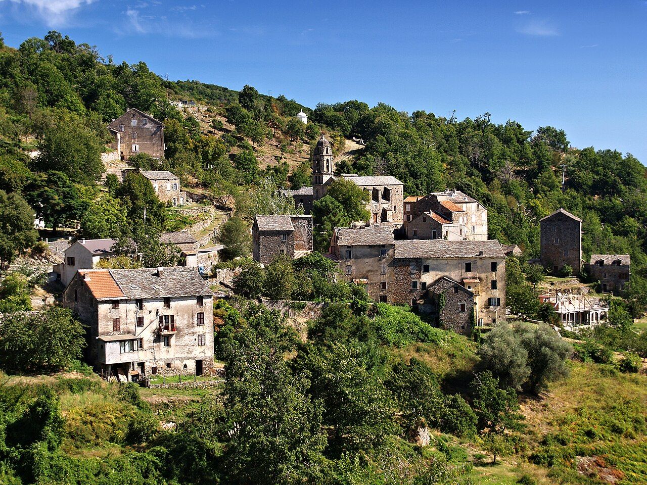 Le village de Zuani, ses maisons de pierre aux toits de lauze et le clocher de l’église, étagés sur une pente boisée